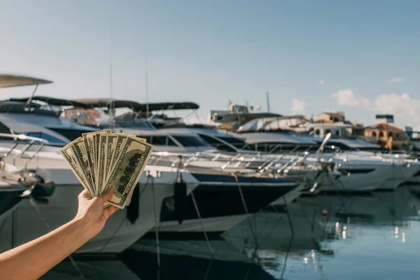 Vista recortada de la mujer sosteniendo billetes de dólar cerca de yates en el mar Mediterráneo - foto de stock