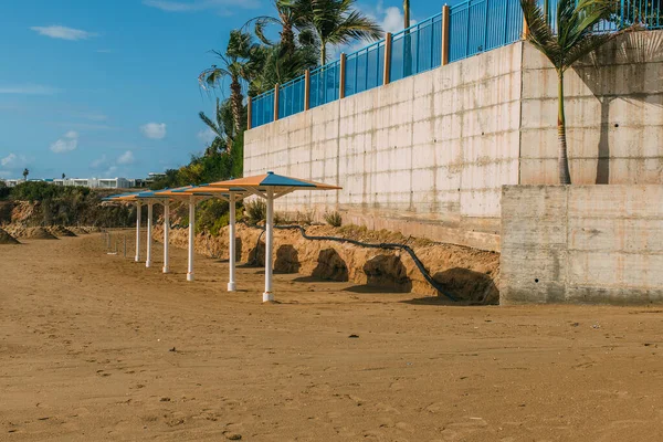 Outdoor umbrellas on sandy beach near palm trees — Stock Photo
