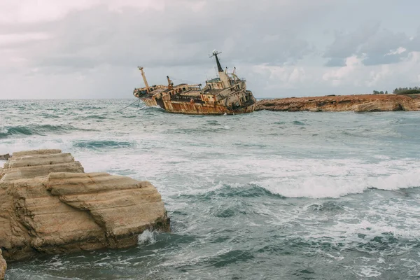 Barco oxidado en el agua del mar Mediterráneo contra el cielo con nubes - foto de stock
