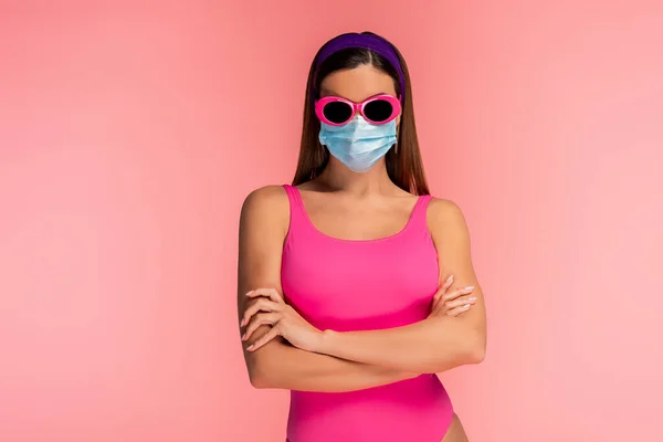 Вид спереду жінки в сонцезахисних окулярах і медична маска з схрещеними руками ізольовані на рожевому — стокове фото