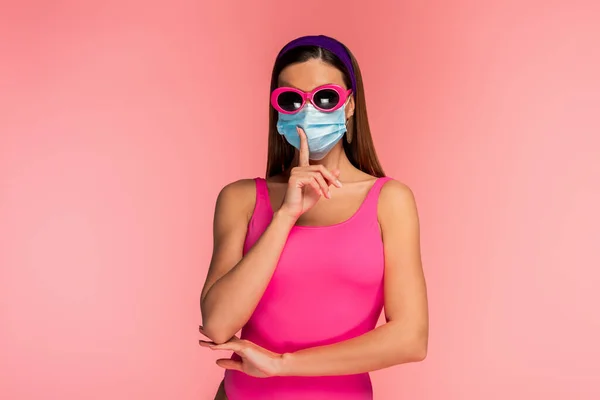 Frontansicht einer Frau mit Sonnenbrille und medizinischer Maske, die ihr Zeichen isoliert auf rosa zeigt — Stockfoto