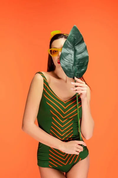 Вид спереди женщины, закрывающей лицо листочком, изолированным оранжевым — стоковое фото