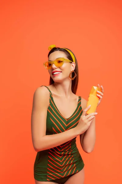 Mulher com protetor solar olhando para longe e sorrindo isolado em laranja — Fotografia de Stock