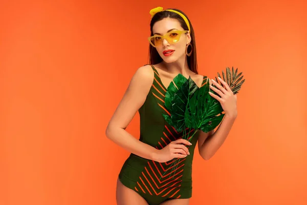 Woman holding leaves and looking at camera isolated on orange — Stock Photo