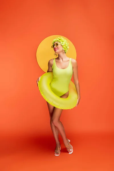 Donna felice in anello nuoto sorridente con cerchio giallo dietro su arancione — Stock Photo