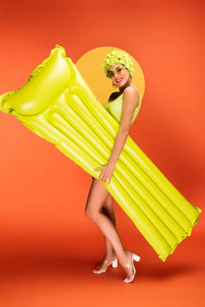 Fille heureuse avec matelas gonflable souriant et regardant la caméra sur fond jaune et orange — Photo de stock