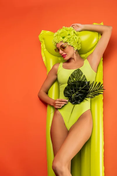 Vista superior de la mujer con hojas verdes sonriendo y acostado en el colchón inflable en naranja - foto de stock