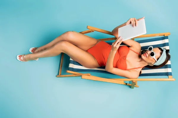 Top view of woman smiling and looking at digital tablet on deckchair on blue — Stock Photo