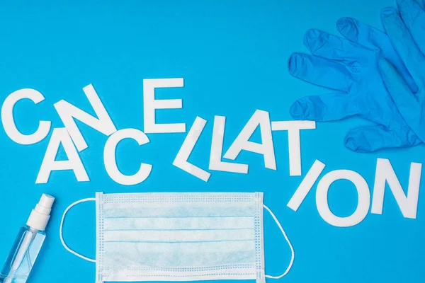 Top view of lettering cancellation near medical mask, bottle of hand sanitizer and latex glove on blue background — Stock Photo