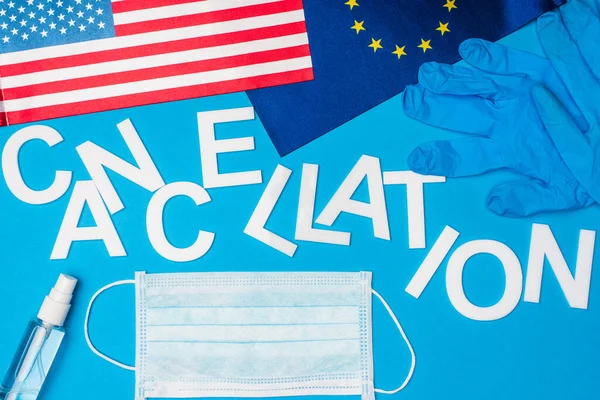 Top view of lettering cancellation near medical mask, latex gloves and flags of european unity and america on blue background — Stock Photo