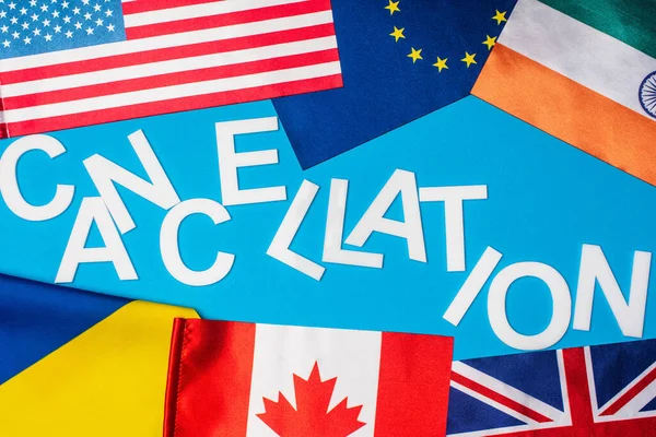 Top view of lettering cancellation near flags of countries on blue surface — Stock Photo