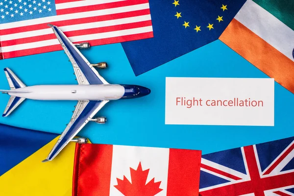 Top view of toy plane near card with flight cancellation lettering and flags of countries on blue surface — Stock Photo