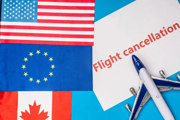 Top view of flags of canada, european union and america near toy plane with flight cancellation lettering on card on blue surface — Stock Photo