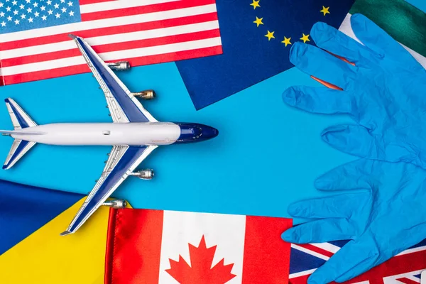 Vista superior de bandeiras de países com luvas de látex e avião de brinquedo em fundo azul — Fotografia de Stock