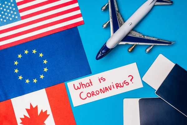 Top view of flags of countries near toy plane and card with what is coronavirus lettering on blue surface — Stock Photo