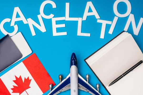 Vista superior del avión de juguete, letras de cancelación cerca de la bandera de Canadá y pasaporte con billete de avión sobre fondo azul - foto de stock