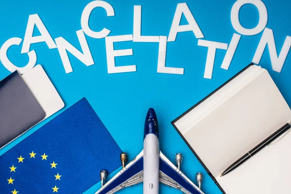 Vista superior de la cancelación de letras cerca de avión de juguete, bandera de la unidad europea y pasaporte con billete de avión sobre fondo azul - foto de stock