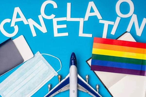 Top view of toy plane, passport near medical mask with lgbt flag and lettering cancellation on blue background — Stock Photo