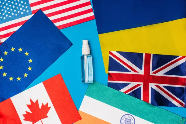 Top view of bottle of hand disanitizer near flags of countries on blue background — стоковое фото