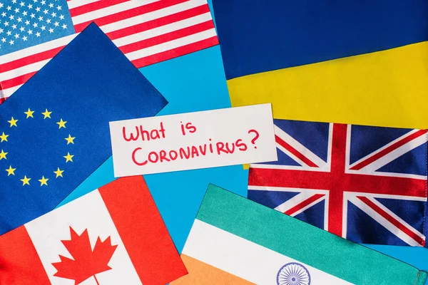 Vue du dessus de la carte avec ce qui est lettrage coronavirus près des drapeaux des pays sur fond bleu — Photo de stock