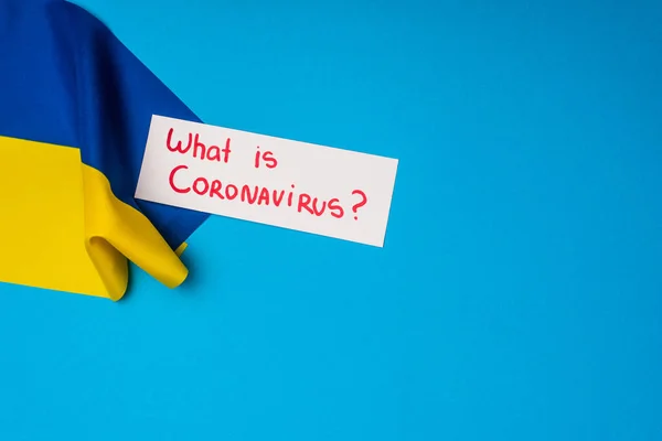 Vista superior de la tarjeta con lo que es la inscripción coronavirus cerca de la bandera de Ucrania sobre fondo azul - foto de stock