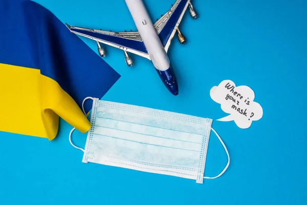 Top view of toy airplane near medical mask, flag of ukraine and speech bubble with where is your mask lettering on blue surface — Stock Photo