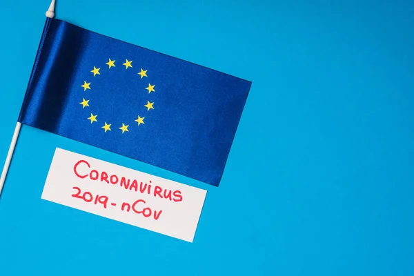 Top view of flag of european unity and card with coronavirus 2019-nCov lettering on blue background — Stock Photo