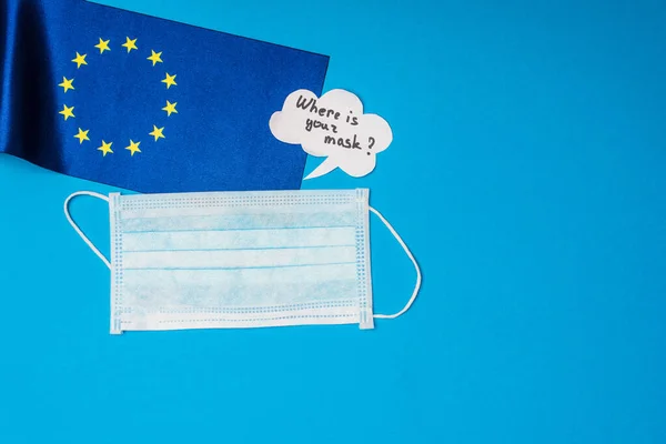 Vista superior de la máscara médica, la bandera de la unidad europea y la burbuja del habla con ¿dónde está su inscripción máscara en la superficie azul - foto de stock