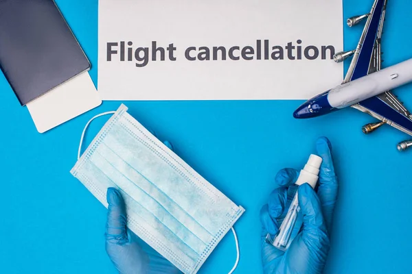 Top view of doctor holding medical mask and hand sanitizer near card with flight cancellation lettering and toy airplane on blue background — Stock Photo