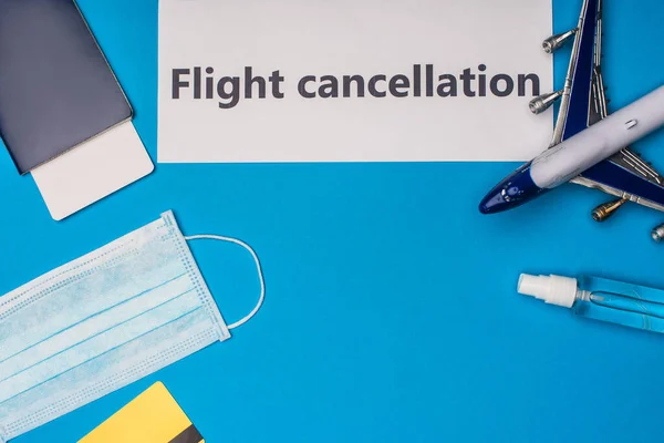 Top view of card with flight cancellation lettering near medical mask, toy airplane, passport and air ticket on blue background — Stock Photo