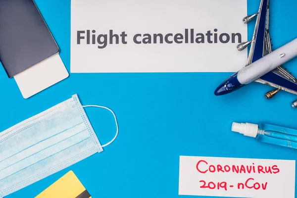 Вид сверху на карты с отменой рейса и коронавирусом 2019-nCov, лежащие рядом с медицинской маской, кредитной картой и игрушечным самолетом на синей поверхности — стоковое фото