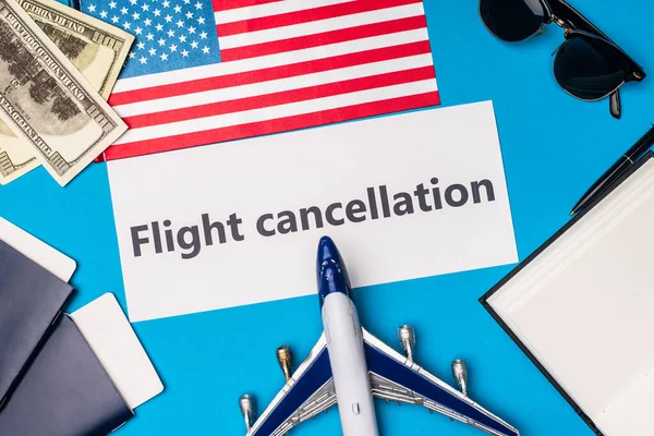 Vista superior de la tarjeta con letras de cancelación de vuelo cerca de avión de juguete, dólares y bandera de América sobre fondo azul - foto de stock