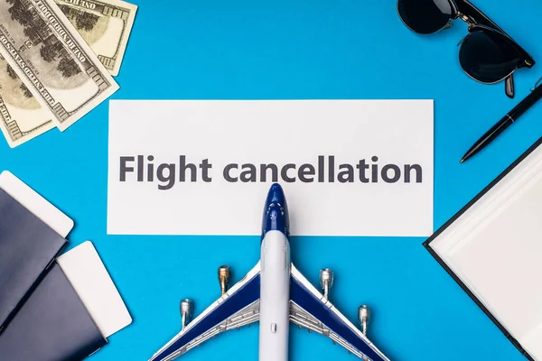 Top view of toy plane near card with flight cancellation lettering, passports and dollar banknotes on blue surface — Stock Photo