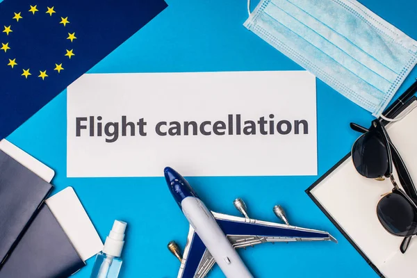 Vista superior de la tarjeta con letras de cancelación de vuelo cerca de la bandera de la unidad europea, avión de juguete y máscara médica sobre fondo azul - foto de stock