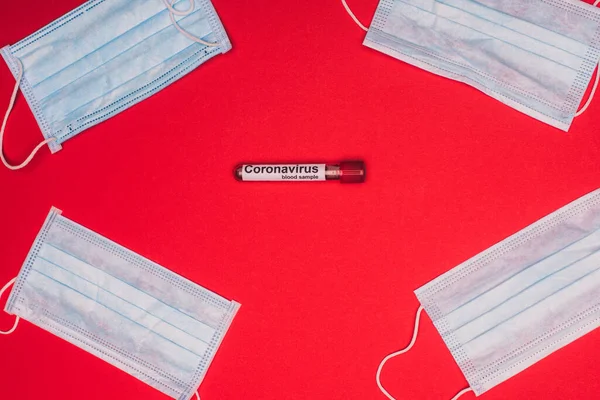 Vue du dessus du tube à essai avec échantillon de sang et inscription du coronavirus près des masques médicaux sur fond rouge — Photo de stock