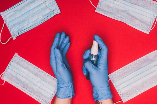 Vista superior del médico sosteniendo el desinfectante de manos cerca de máscaras médicas sobre fondo rojo - foto de stock