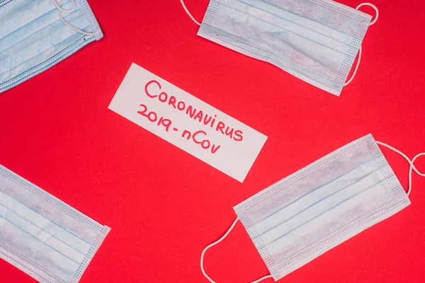 Vista superior de la tarjeta con letras coronavirus 2019-nCov cerca de máscaras médicas sobre fondo rojo - foto de stock