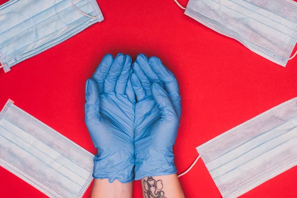 Visão superior de mãos de médico perto de máscaras médicas no fundo vermelho — Fotografia de Stock