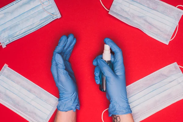 Vista superior del médico usando desinfectante de manos cerca de máscaras médicas sobre fondo rojo - foto de stock