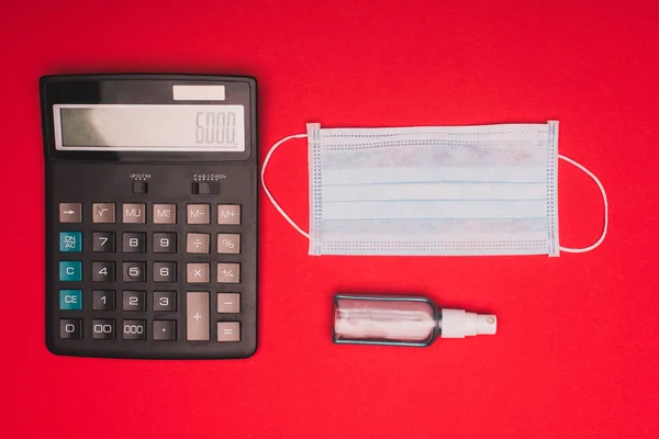 Vue du dessus de la calculatrice, masque médical et désinfectant pour les mains sur fond rouge — Photo de stock