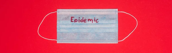 Draufsicht auf medizinische Maske mit Epidemie-Schriftzug isoliert auf Rot, Panoramaaufnahme — Stockfoto
