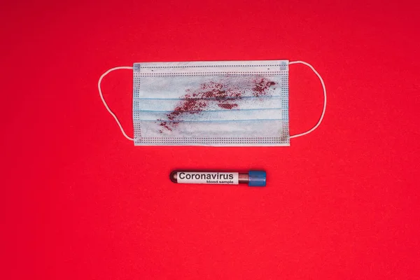 Vista superior de la máscara con sangre y probeta con muestra de sangre y letras de coronavirus sobre fondo rojo - foto de stock