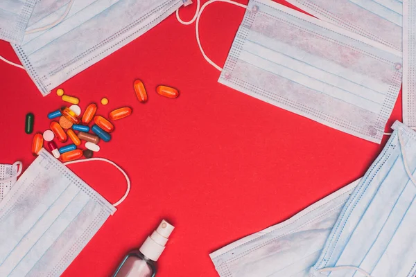 Top view of hand sanitizer near pills and medical masks on red background — Stock Photo