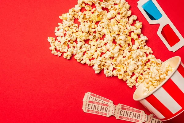 Vista superior de palomitas de maíz, entradas de cine y gafas 3D sobre fondo rojo - foto de stock