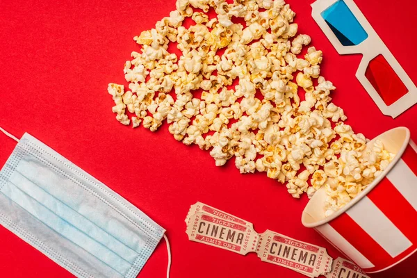 Vue du dessus du masque médical, billets de cinéma avec pop-corn et lunettes 3D sur fond rouge — Stock Photo