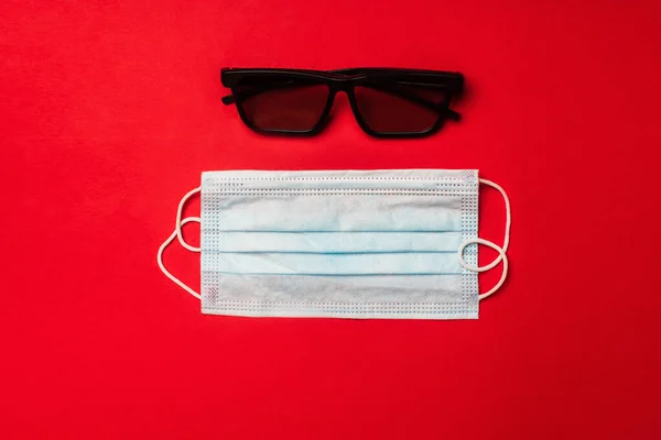 Draufsicht auf medizinische Maske und Sonnenbrille auf rotem Hintergrund — Stockfoto