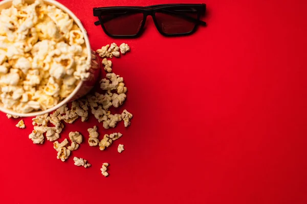 Top view of sunglasses near bucket with tasty popcorn on red background — Stock Photo