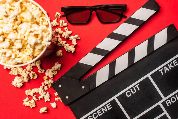 Top view of clapperboard near bucket with popcorn ans sunglasses on red background — Stock Photo