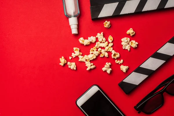 Vue du dessus du smartphone près de clapperboard, pop-corn et désinfectant pour les mains sur fond rouge — Photo de stock