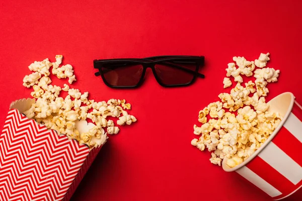 Sonnenbrille neben Eimern mit Popcorn auf rotem Hintergrund — Stockfoto